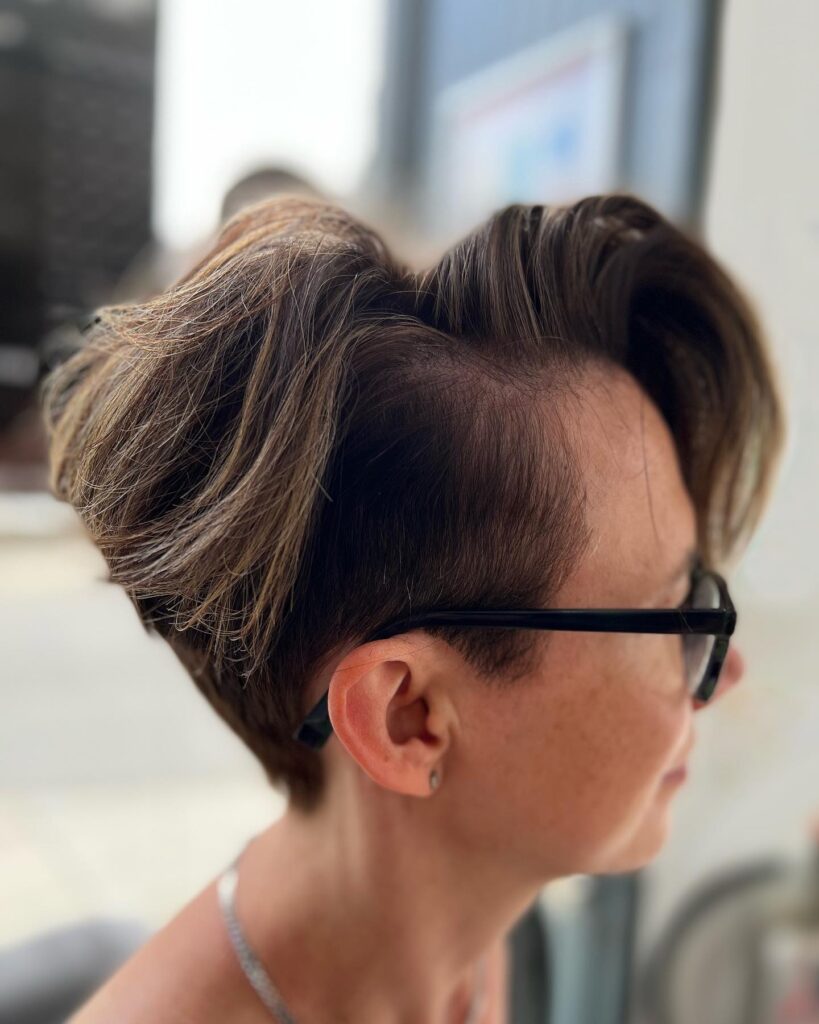 A woman in profile with a voluminous dark brown quiff featuring caramel highlights and short tapered sides.