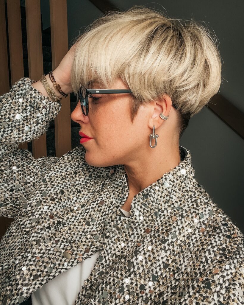 A woman over 60 with a rounded blonde mushroom bob featuring a dark buzzed nape undercut.