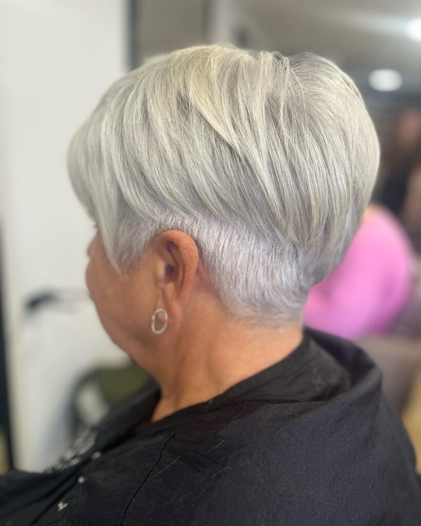 A woman over 60 with a straight silver bowl-style pixie cut and a closely tapered undercut.