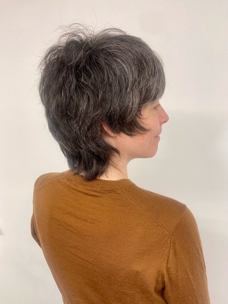 A woman over sixty from a side profile wearing a short dark brunette shag with natural silver highlights and choppy crown layers.