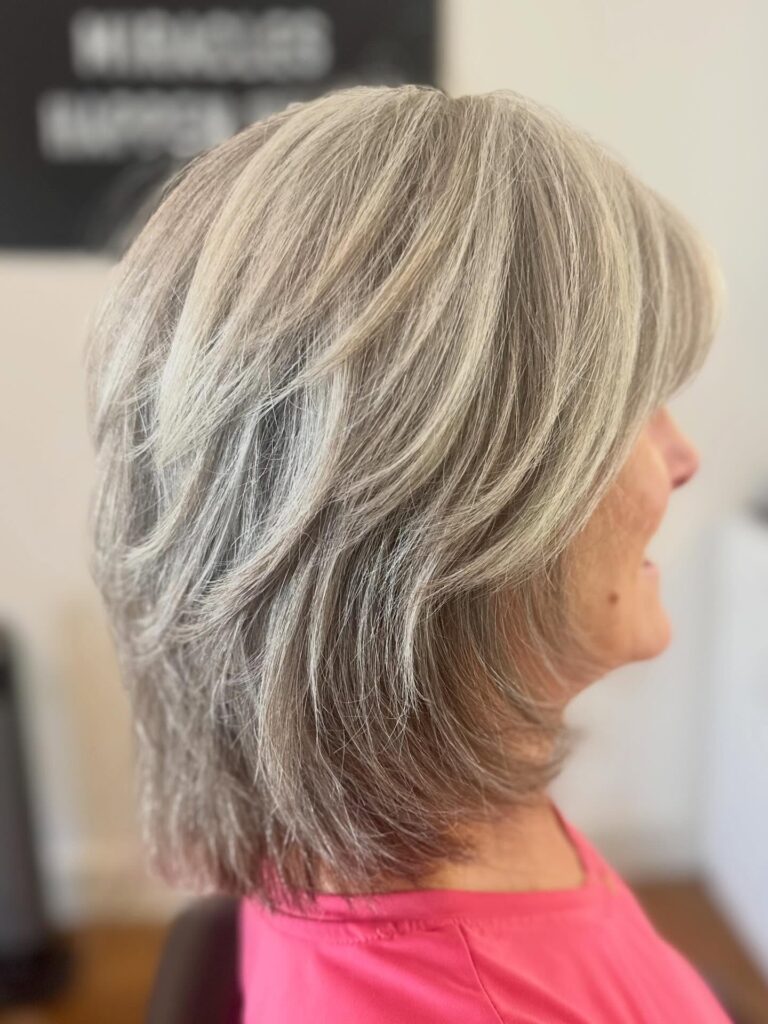 A woman with a medium-length ashy silver feathered shag hairstyle featuring soft sweeping layers.