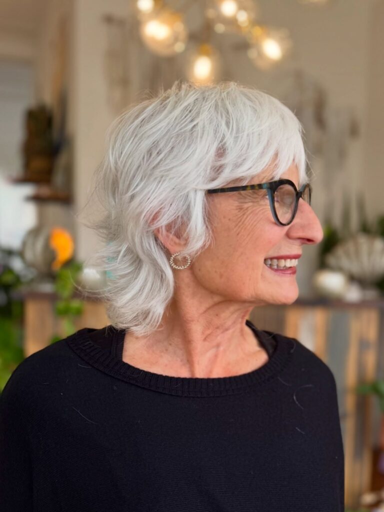 A woman over sixty with a short white shag haircut featuring side-swept bangs and flipped-out layers at the nape.