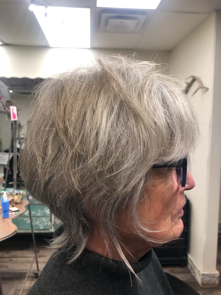 A woman with a short steel-grey layered shag hairstyle that is stacked in the back with longer wispy pieces in front.
