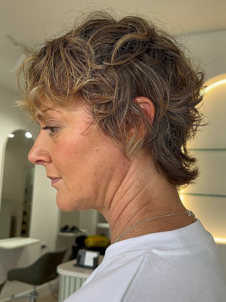 A woman with a short wavy shag hairstyle in a warm caramel brown color with golden highlights and piecey layers.