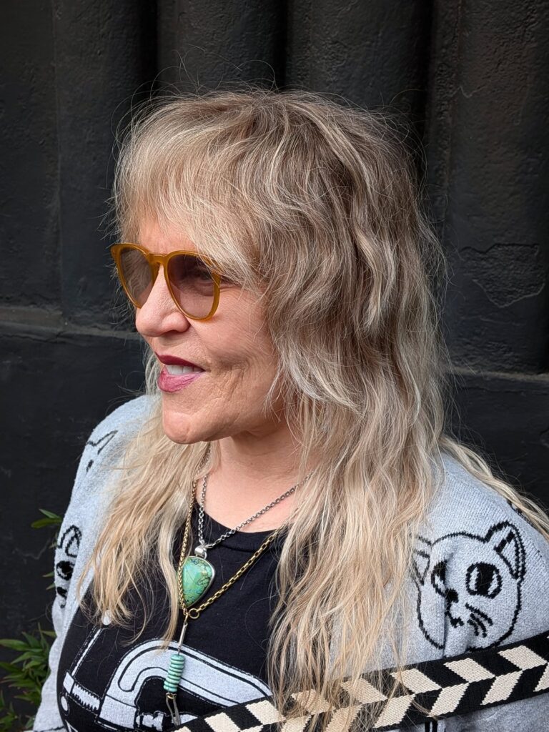 A woman over sixty with a long sandy blonde shag haircut featuring a heavy fringe and beachy waves.