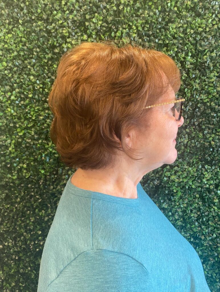 A woman over sixty from a side profile with a short auburn shag haircut featuring stacked layers and a rounded shape.
