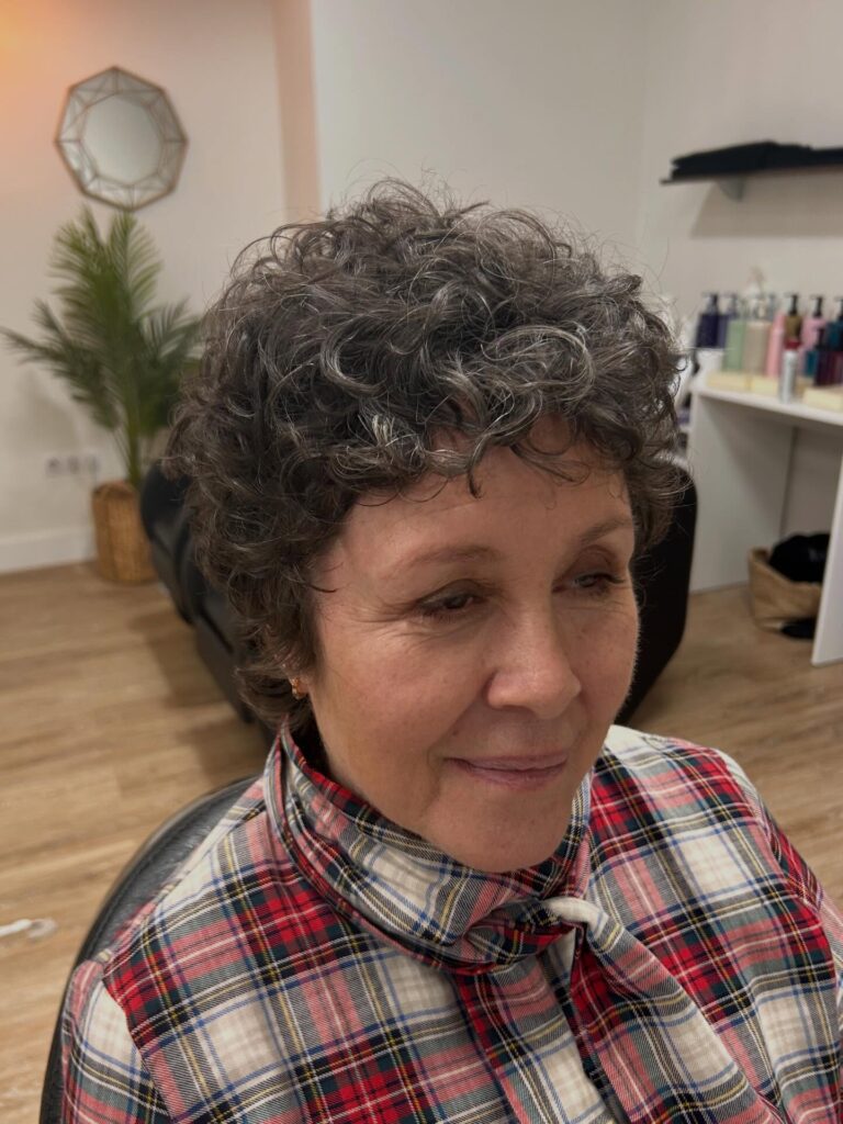 A woman over sixty with a short, curly salt-and-pepper shag haircut featuring tight ringlets and a soft fringe.