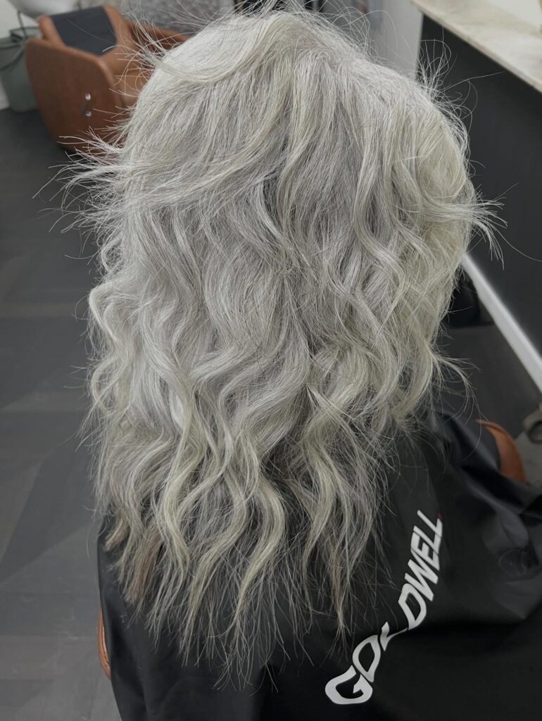 A rear view of a woman with long, silver, wavy hair in a layered shag style featuring soft texture.