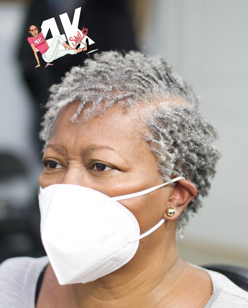 A close-up of an older Black woman with a short hairstyle consisting of small, perfectly defined silver finger coils.