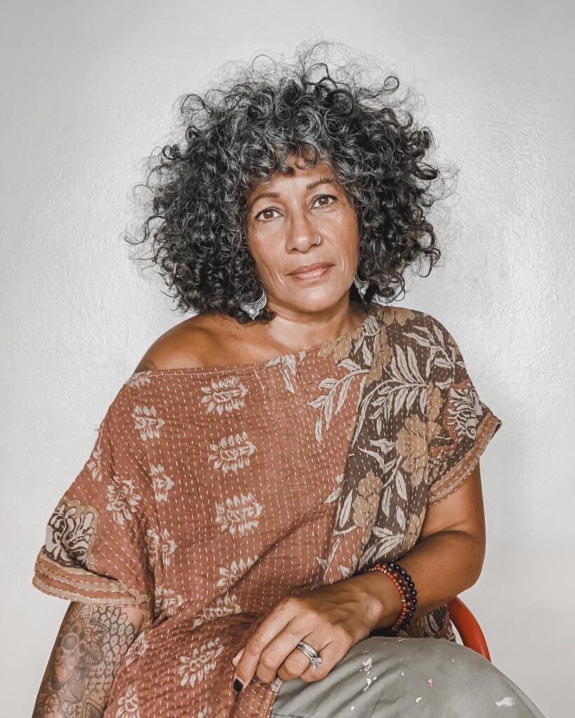 A black woman over 60 with a big and voluminous shoulder-length curly hairstyle in a salt-and-pepper color with curly bangs.