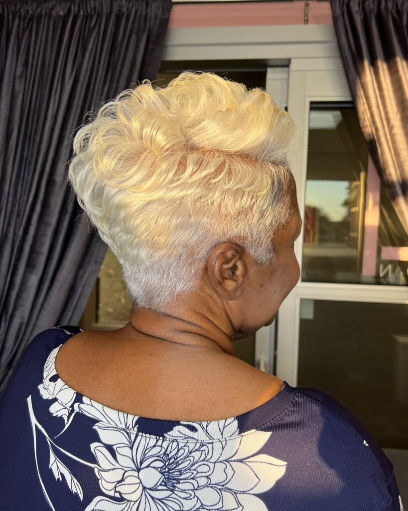 A side and back view of a woman featuring a bright platinum blonde pixie cut with soft waves on top and tapered silver sides.