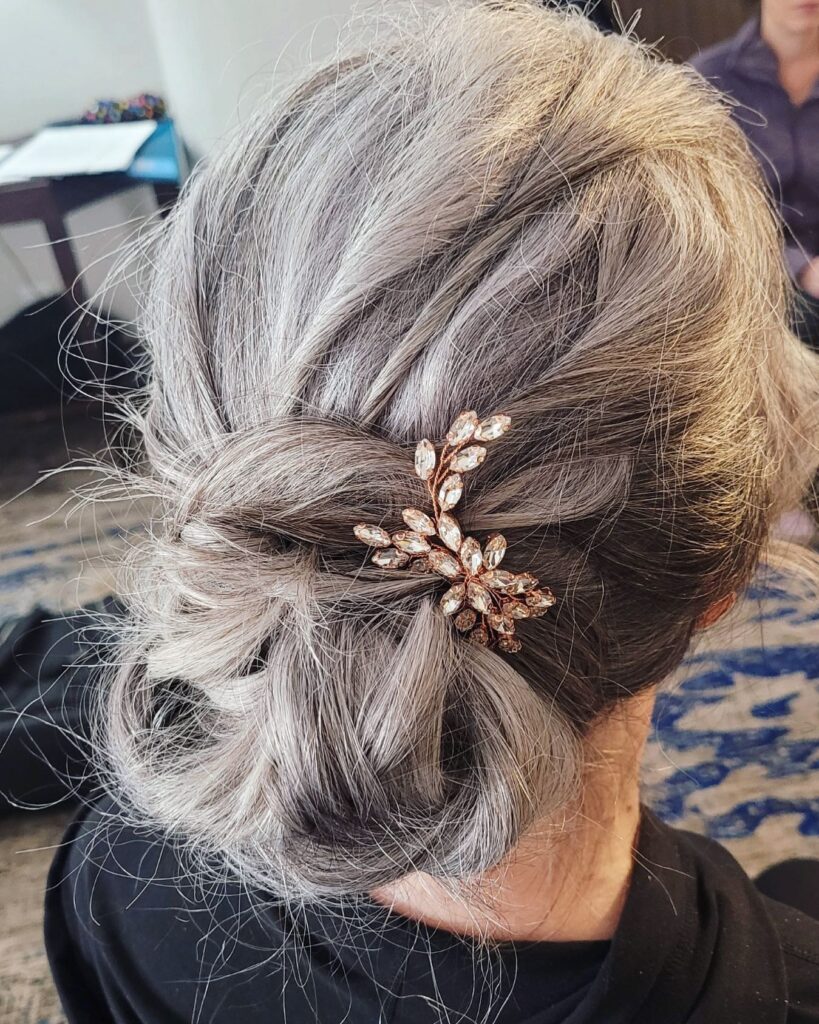 A close-up from behind of a woman with silver hair styled in a loose, low knot and decorated with a crystal leaf hair vine.