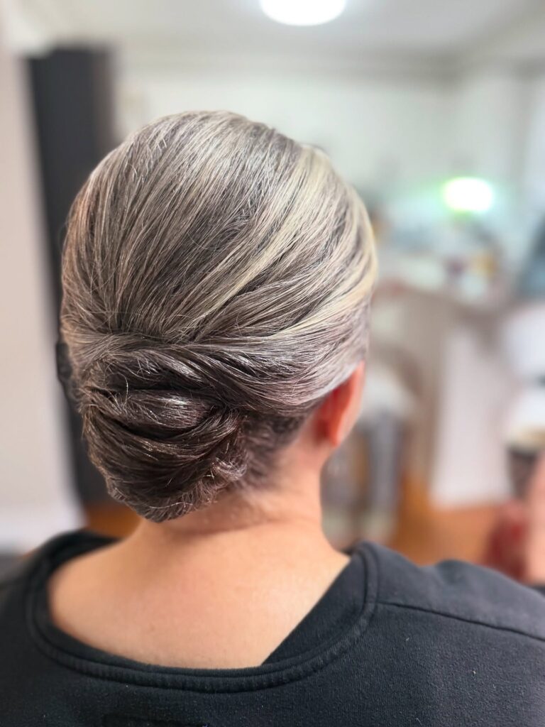 A back view of a woman with salt-and-pepper hair styled into a sleek and neatly wrapped low chignon.