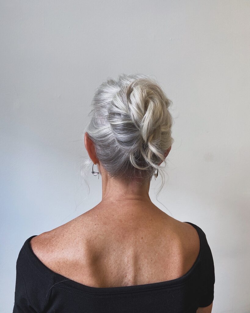 A woman with silver hair styled in a soft and airy vertical tuck-updo with loose wispy strands.