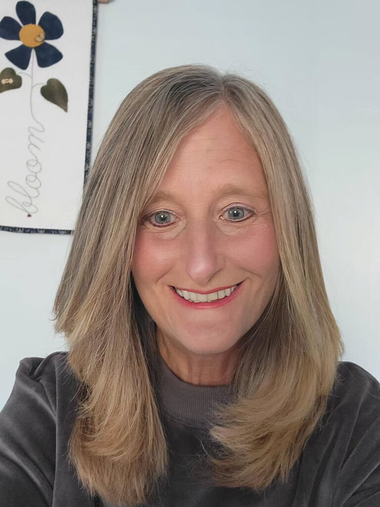A woman with shoulder-length ash blonde hair featuring long layers and inward-curved ends.