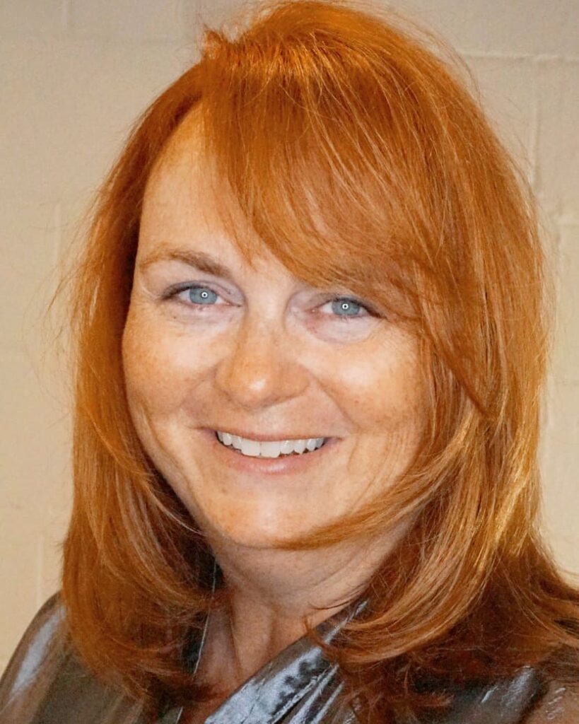 A woman with medium-length bright copper red hair and side-swept bangs.