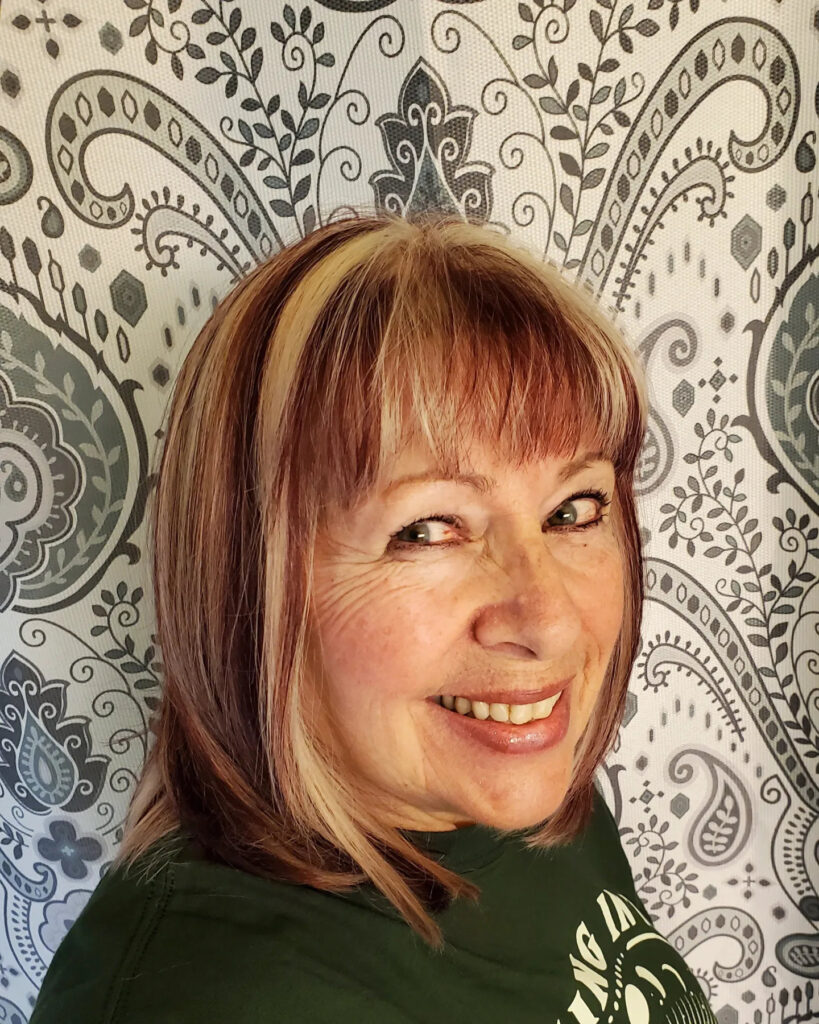 A middle-aged woman with a collar-length multitonal bob and straight bangs smiling warmly.