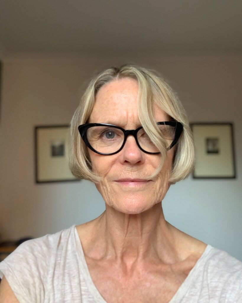 A woman wearing black glasses with a stylish ash-blonde French bob that curves toward the jawline.