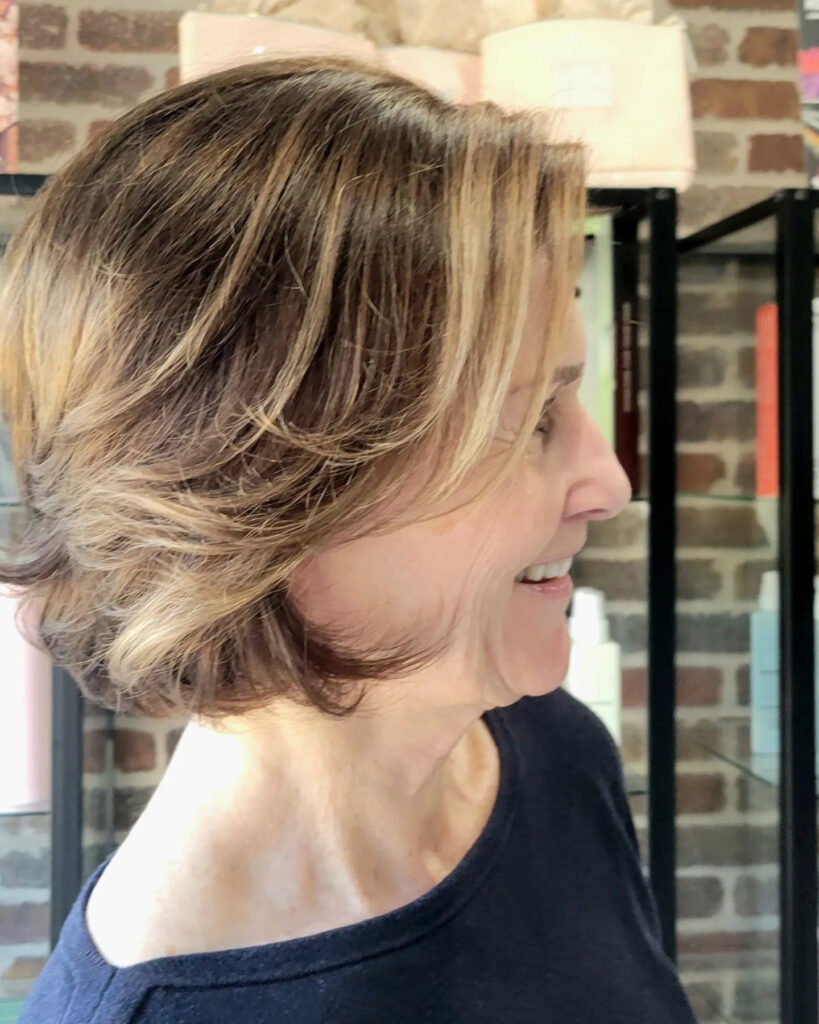 A woman in profile showing off a neck-length layered haircut with warm caramel balayage highlights.