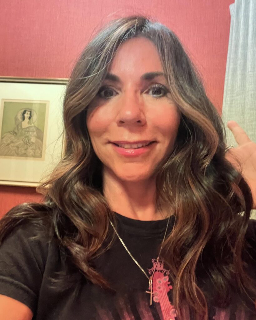 A woman with long, wavy, deep brown hair featuring warm caramel balayage highlights throughout the ends.