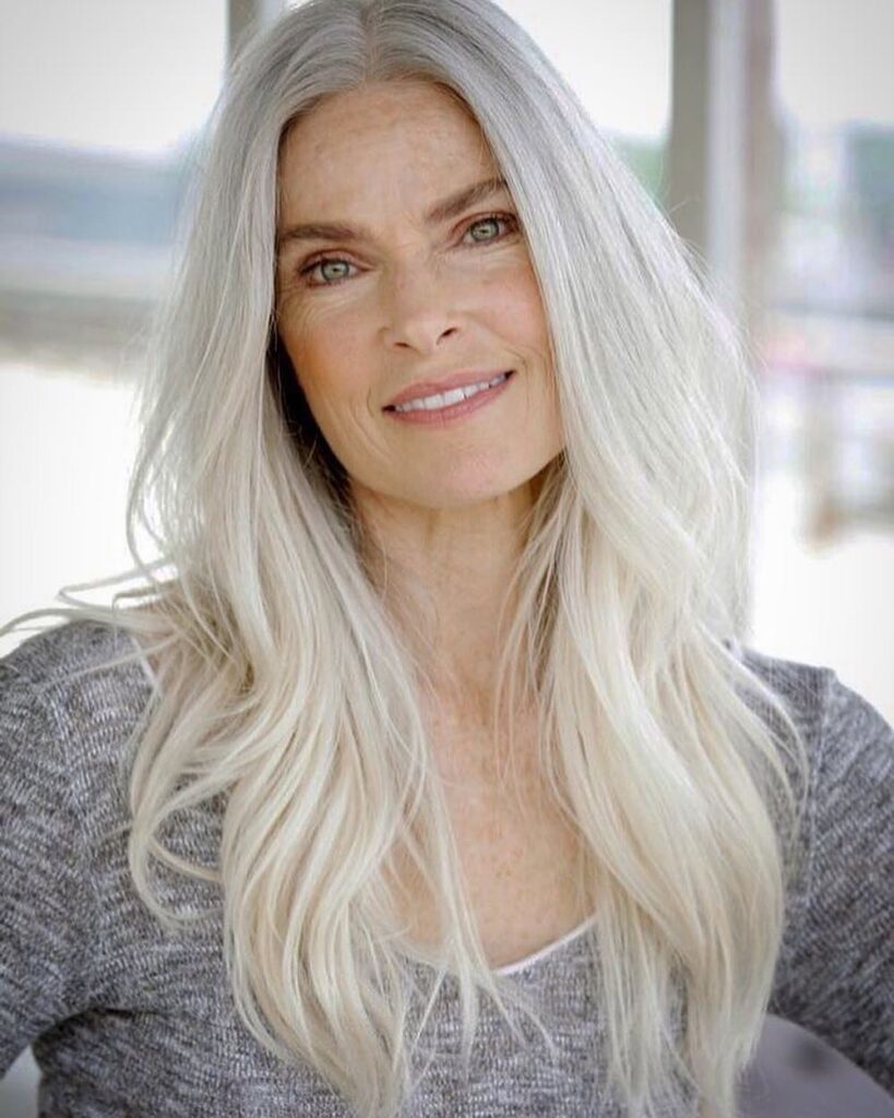A woman with long, layered, icy silver and white hair styled in soft waves.