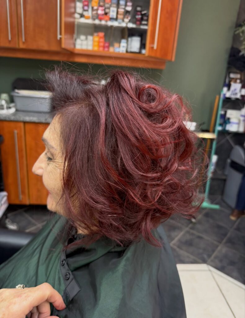 A woman with a voluminous burgundy bob styled with bouncy curls and layers.