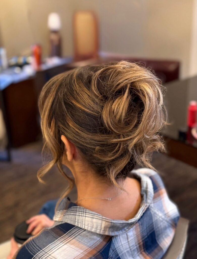 A woman from behind with a textured, messy updo featuring golden highlights and loose tendrils.