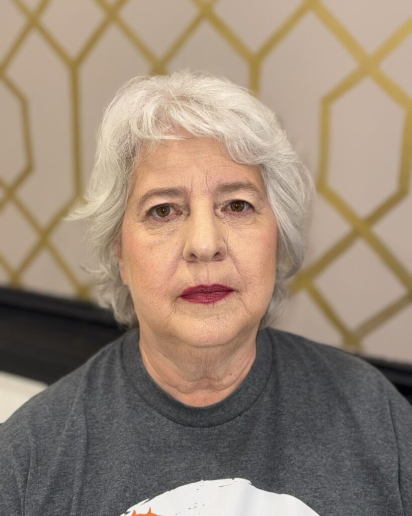 A woman with a soft, feathered silver pixie cut and a light, wispy fringe.