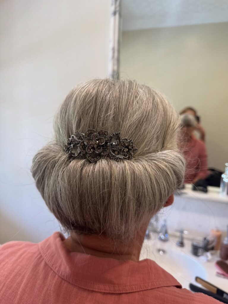 A woman from behind with a sleek silver chignon updo accented by a large jeweled floral barrette.