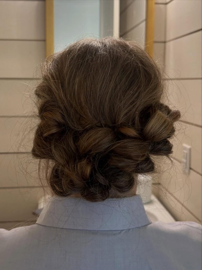 A textured brown updo for women over 60, loosely braided and pinned low at the neck, featuring subtle highlights.