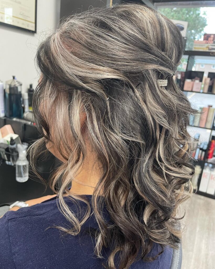 A textured medium-length brown and silver half-up hairstyle for women over 60, featuring loose waves secured at the back with a sparkling crystal clip.