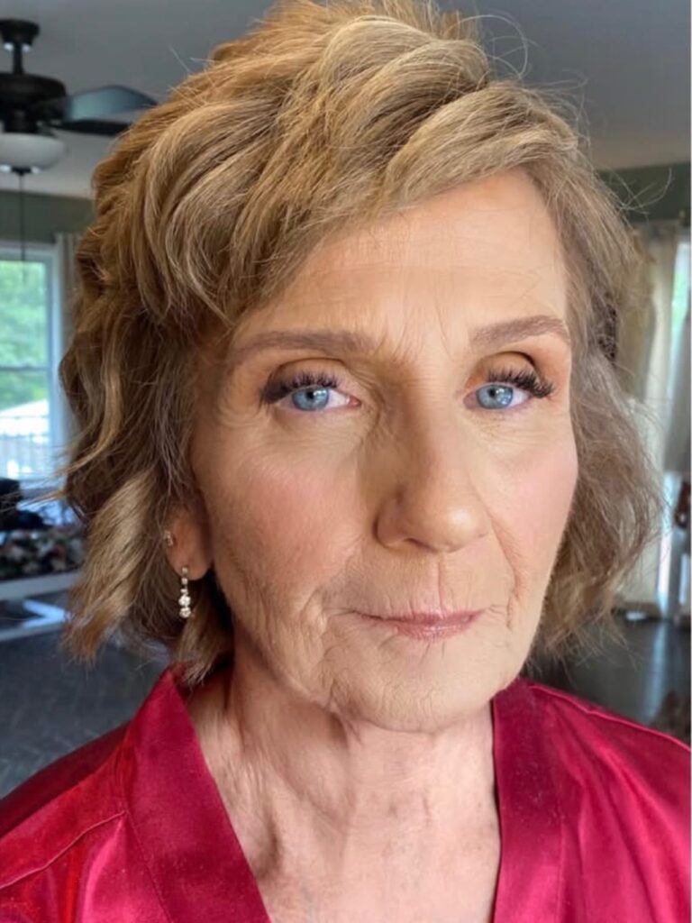 A woman over 60 with a short honey blonde bob featuring soft textured waves and side-swept bangs.