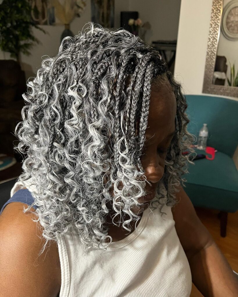 A woman wearing silver and black shoulder-length braids that end in tight, defined curls.