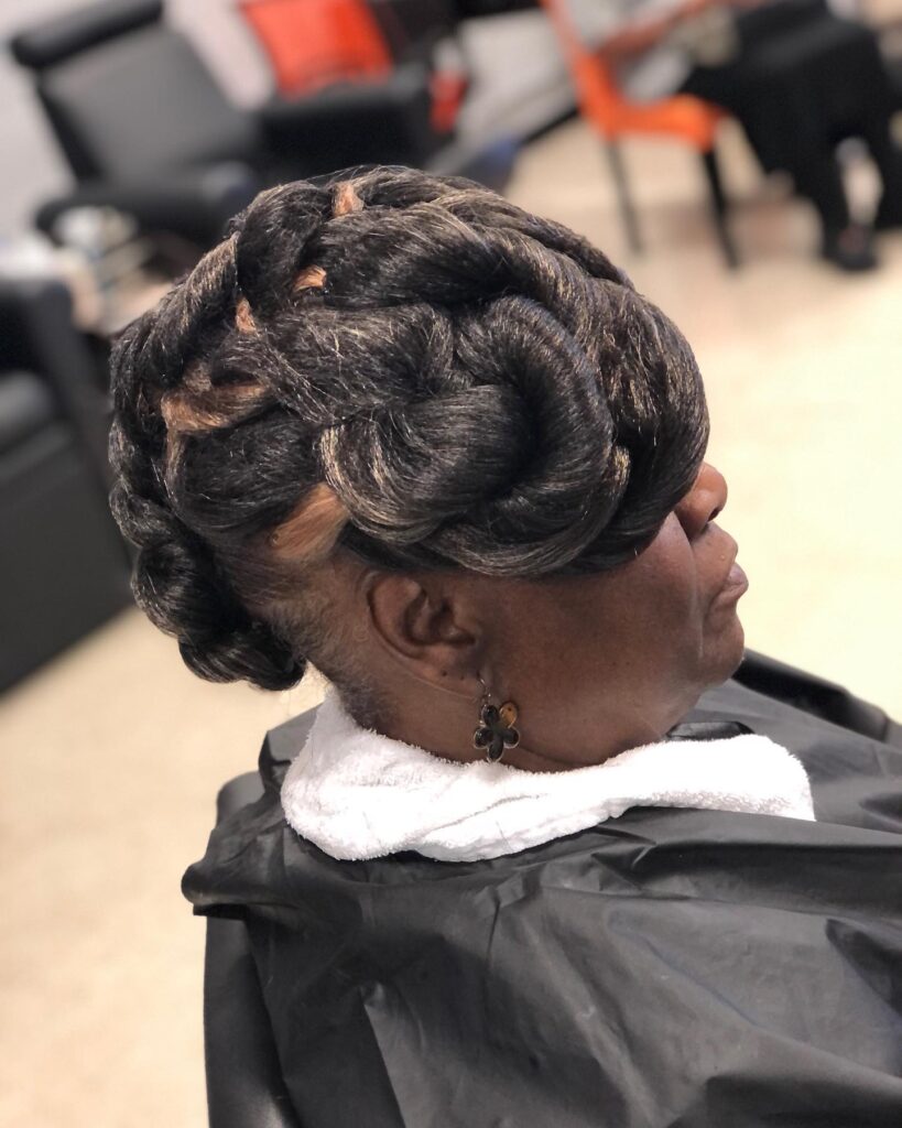 A woman wearing an intricate updo made of thick dark twists with golden highlights sculpted into a crown.