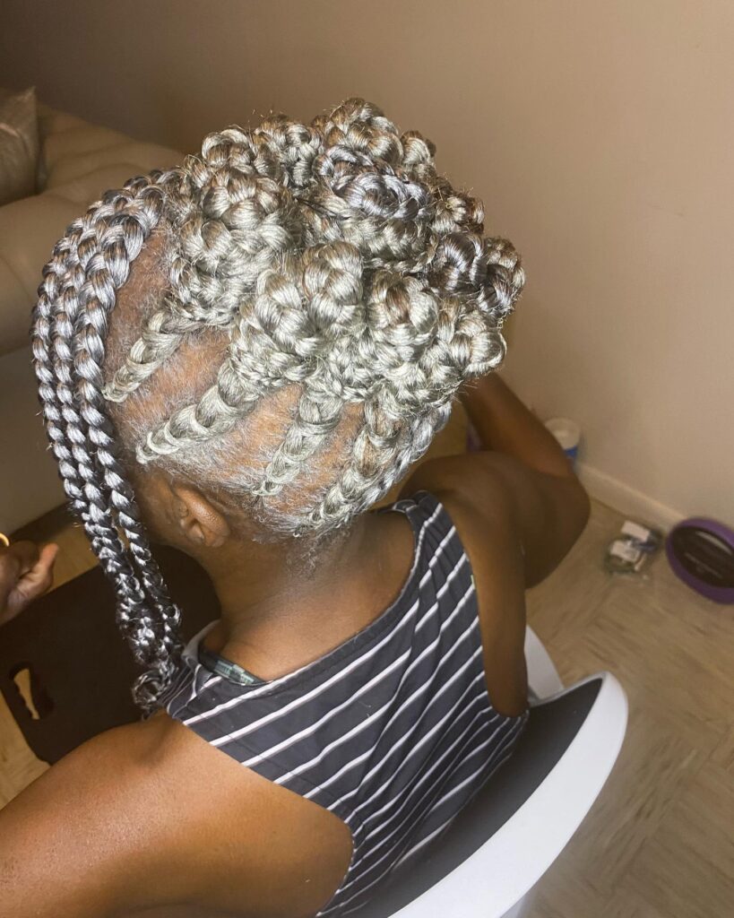 A woman viewed from the back wearing a silver braided updo with thick cornrows gathered into a high bun.