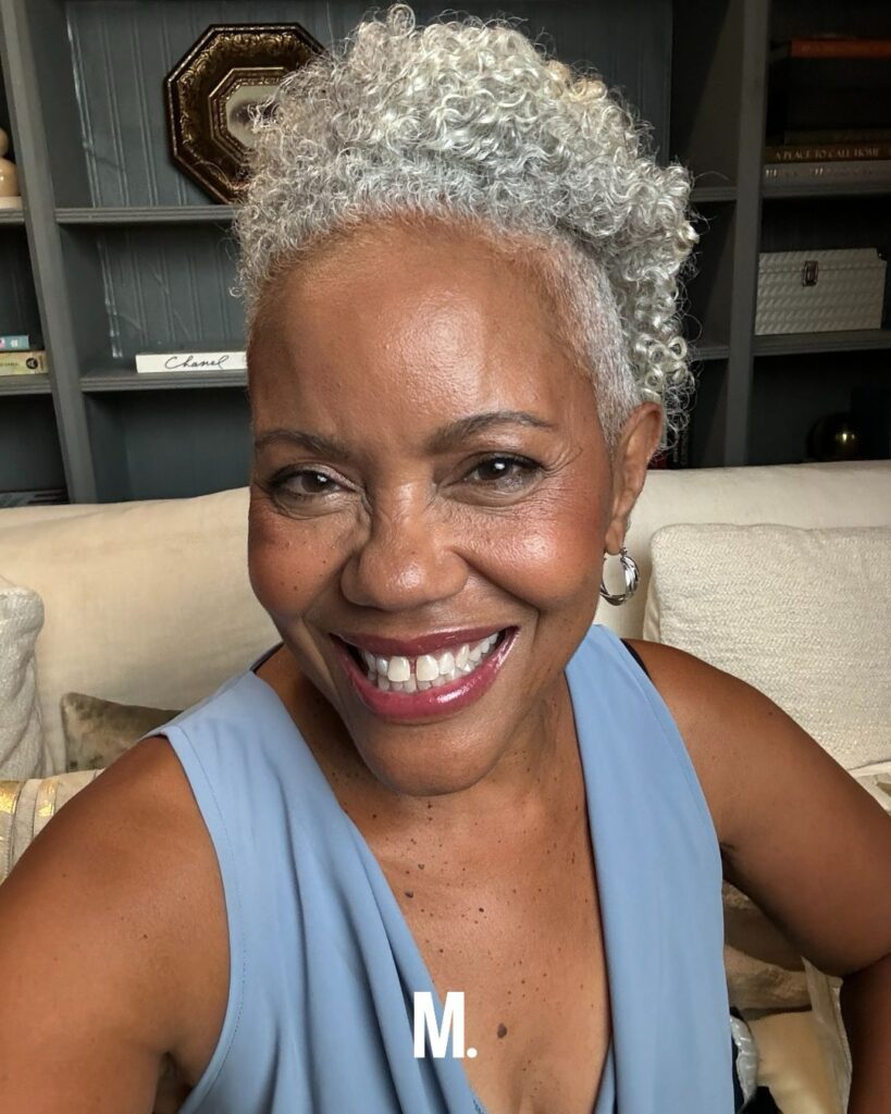 A smiling woman with a short, tapered natural hairstyle featuring tight silver and white curls with volume at the top.