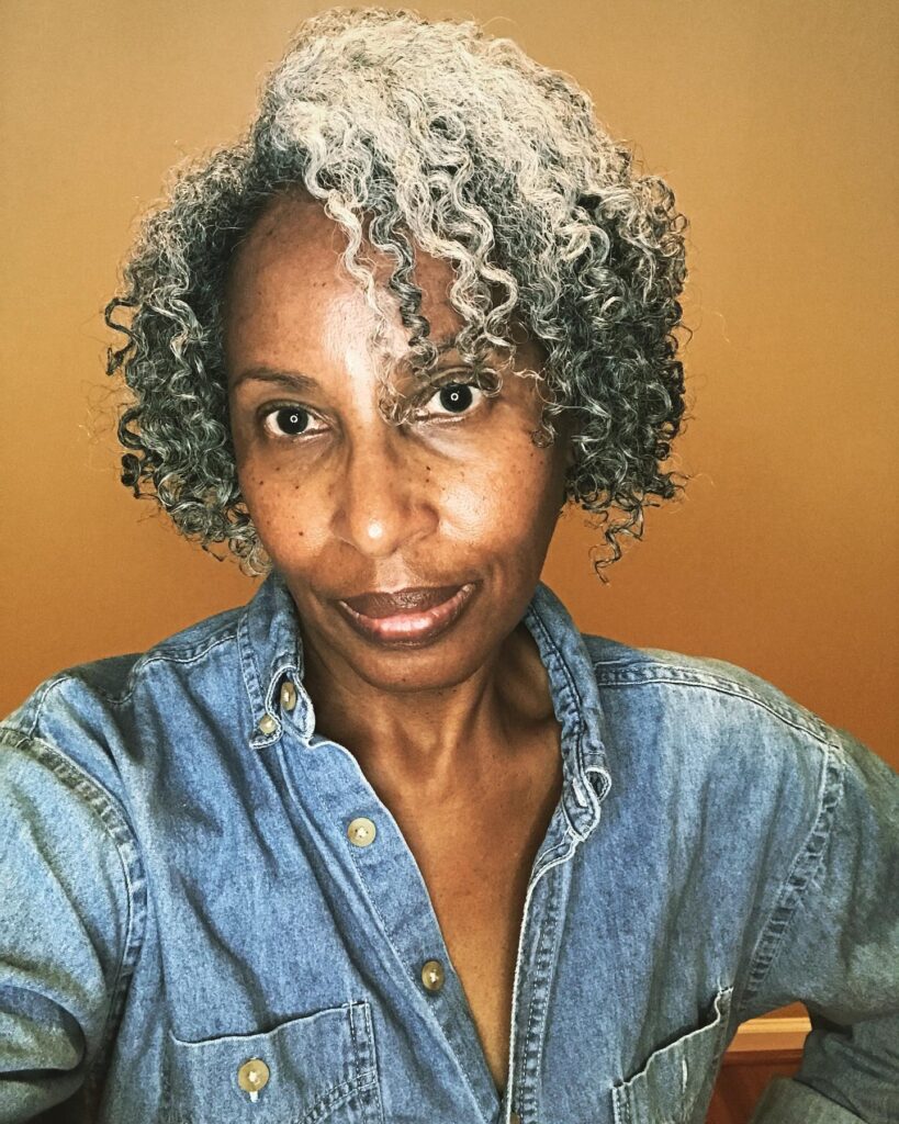 A woman with a chin-length curly bob featuring a vibrant mix of silver and dark grey natural ringlets.