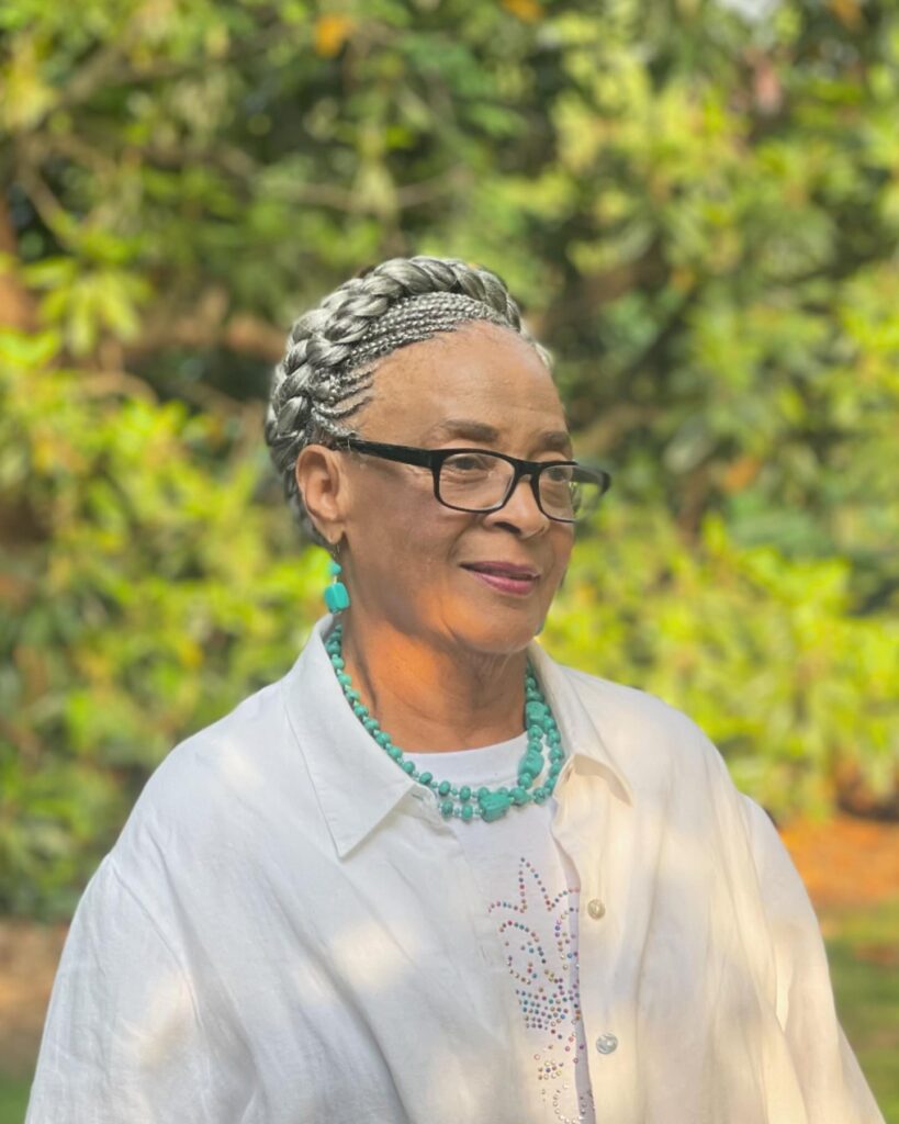 A woman over 60 with a large silver braided crown updo and smaller cornrows underneath.