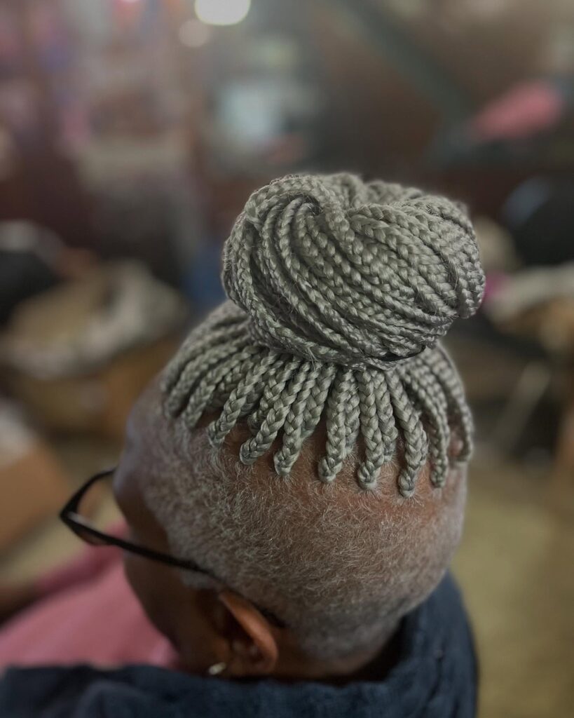 A woman over 60 with a short, silver, buzzed haircut and a large braided bun styled on top of her head.
