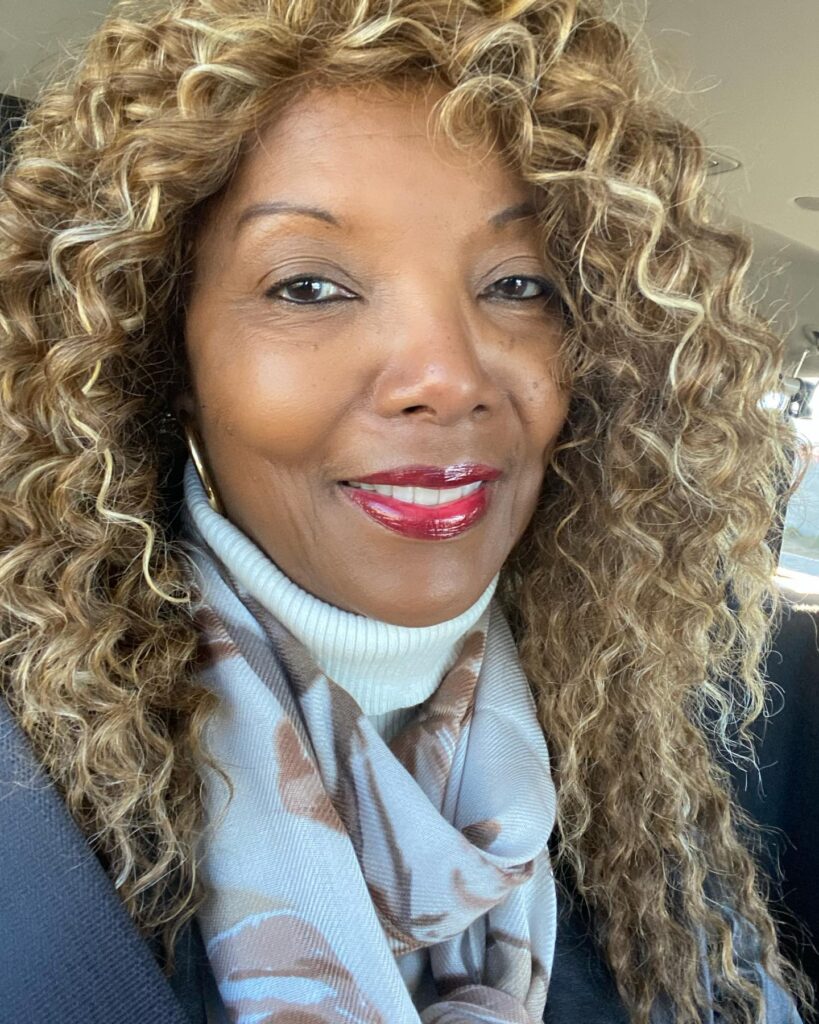 A woman over 60 with long voluminous curls in a bright honey blonde and caramel color.