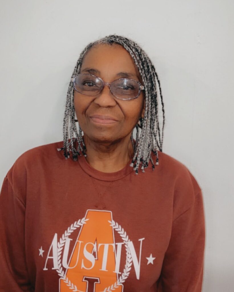 A woman over 60 with shoulder-length salt-and-pepper individual braids and a side part.