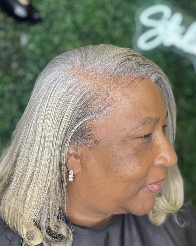 A woman over 60 seen in profile wearing a medium-length silver and gray sew-in with a straight texture and curved-under ends.