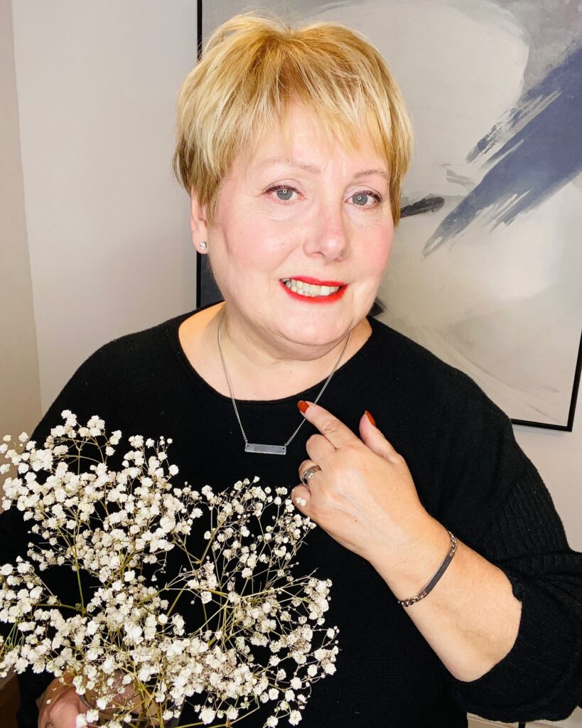 A smiling woman over 60 with a short, spiky honey-blonde pixie cut and soft, wispy bangs.