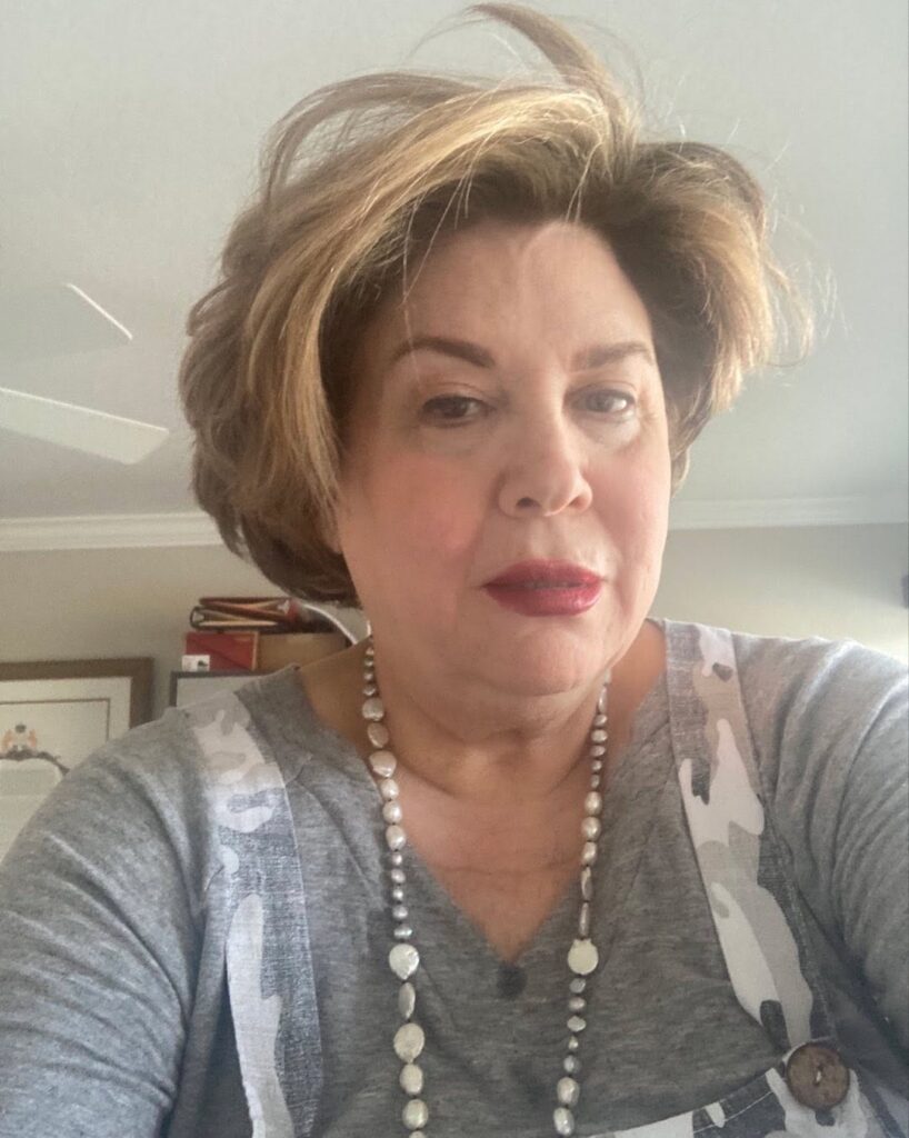 A woman over 60 wearing a voluminous honey-highlighted bob that is swept back from her face.