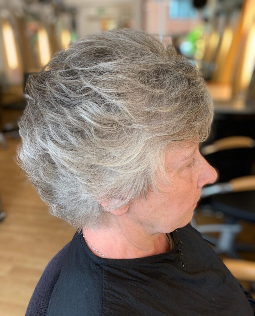 A side profile of a woman with a short feathered silver haircut featuring voluminous layers at the back.