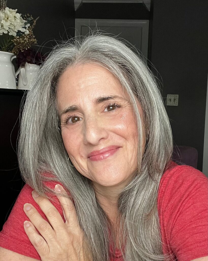 A woman with medium-length straight salt-and-pepper hair that has face-framing layers and a center part.