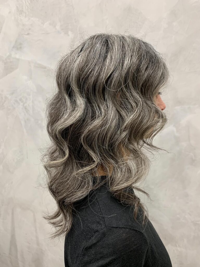 A woman seen from the side with medium-length wavy salt-and-pepper hair and layered ends.