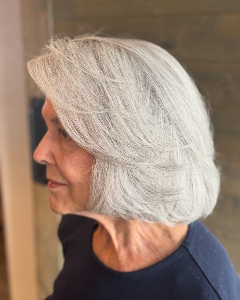 A side view of a woman with a feathery layered silver bob hairstyle.
