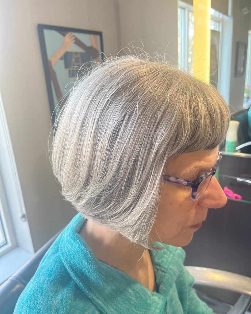A woman in profile wearing a chin-length silver bob with a short micro fringe.