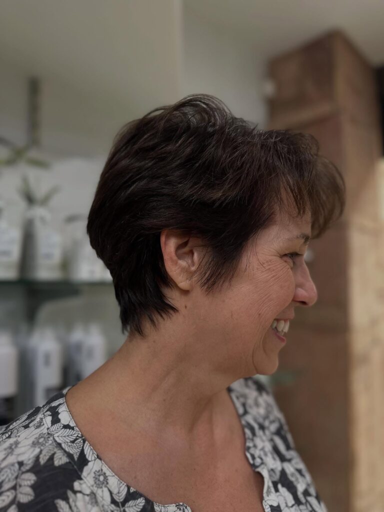 A smiling woman over 60 with a soft espresso brown pixie cut featuring feathered layers and a tapered nape.